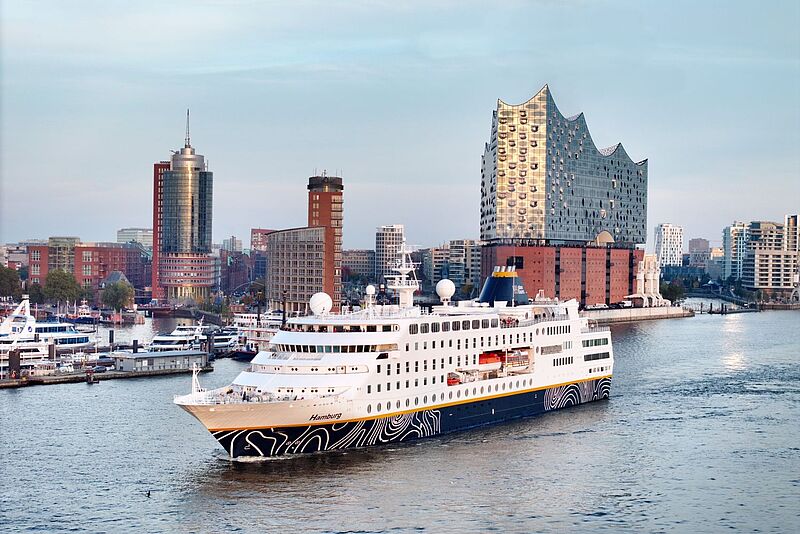 Hamburg ist Ein- und Ausschiffungshafen der neuen Lappland-Route von Plantours. Foto: ck Das kleine Kreuzfahrtschiff Hamburg mit blauweißem Rumpf verlässt den Hafen der gleichnamigen Hansestadt. Im Hintergrund thront vor blauem Himmel die Elbphilharmonie.