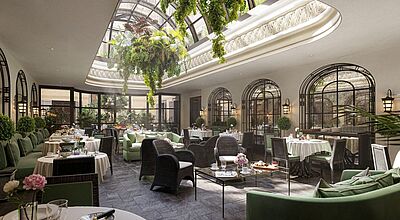 Elegantes Wintergarten-Restaurant im The Carlton Mailand mit üppiger Begrünung, Glasdach und stilvoll gedeckten Tischen