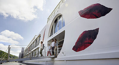 Ein junges, freudiges Elternpaar mit einem Kind verlässt ein Flusskreuzfahrtschiff über die Gangway zum Landgang. 