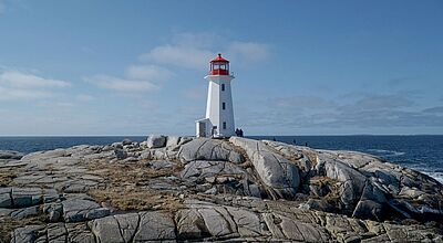 Ein weißer Leuchtturm mit rotem Dach steht auf einer felsigen Landzunge am Meer. Der Himmel ist leicht bewölkt, das Meer ruhig, und einige Menschen spazieren über die glatten, grauen Felsen rund um den Leuchtturm.
