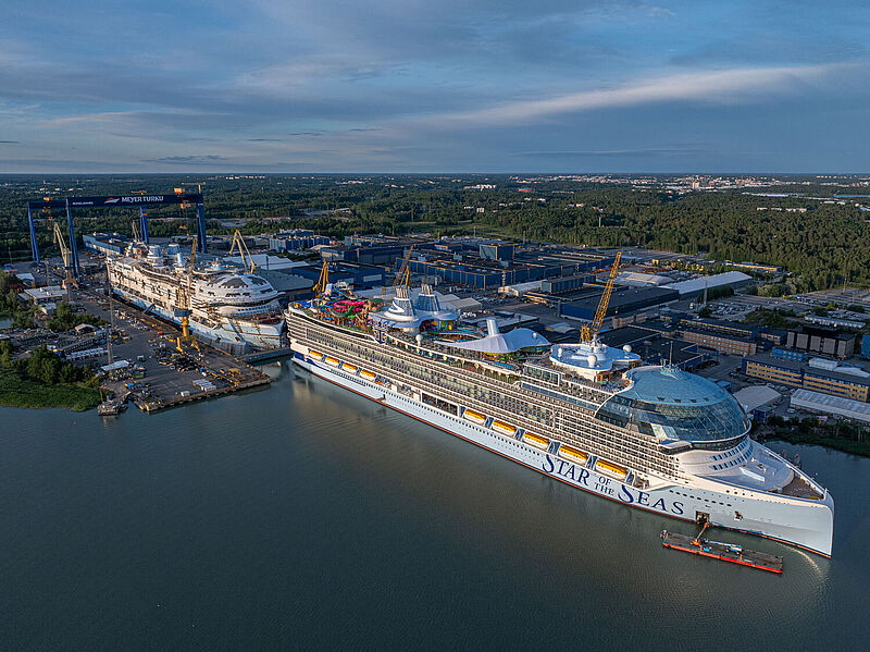 Luftaufnahme einer Werft, in der zwei gigantische baugleiche Kreuzfahrtschiffe liegen. Das hintere ist noch nicht komplett fertiggestellt.