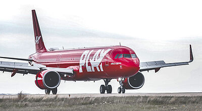 Ein rotes Flugzeug der isländischen Airline Play steht auf einer Startbahn vor weiß-grau bewölktem Himmel