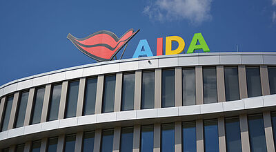 Nahaufnahme der obersten Etage der modernen Aida-Reedereizentrale in Rostock. Auf dem Dach prangen der logohafte Firmenname und der bekannte rote Kussmund.