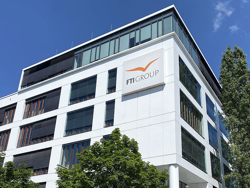 Eckansicht eines modernen Bürogebäudes. Auf der weißen Fassade prangt in orangefarbenen Buchstaben der Firmenname FTI.