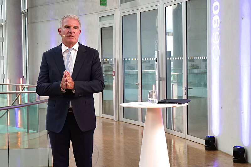 Zufrieden mit dem Geschäft, aber nicht mit der Politik: Lufthansa-Chef Carsten Spohr. Foto: rie Lufthansa-Chef Carsten Spohr steht im Business-Anzug neben einem weißen Rednerpult in einem modernem Konferenzraum in der Lufthansa-Zentrale mit Glasfronten und blauer Beleuchtung.