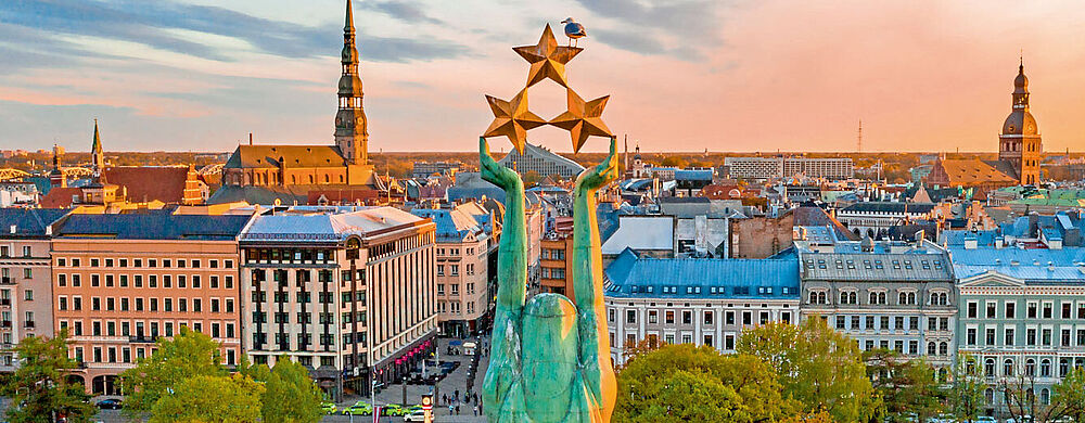 Das Freiheitsdenkmal ist das Wahrzeichen Rigas Stadtpanorama Riga mit Freiheitsdenkmal im Vordergrund, historische Altstadt mit Kirchtürmen, Herbstbäume und Abendhimmel.