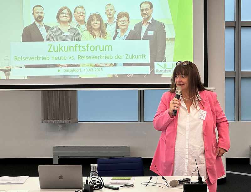 Marija Linnhoff, Chefin des Reisebüro-Verbands VUSR, steht mit einem Mikrofon in der Hand an einem Tisch in einem Konferenzraum und redet