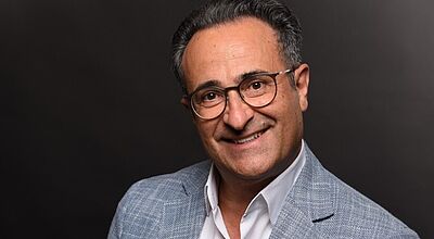 Francisco Sanchez neuer Regional Sales & Marketing Director bei der Sani/Ikos Group Lächelnder Geschäftsmann mit Brille im hellblauen Sakko mit weißem Hemd vor schwarzem Hintergrund