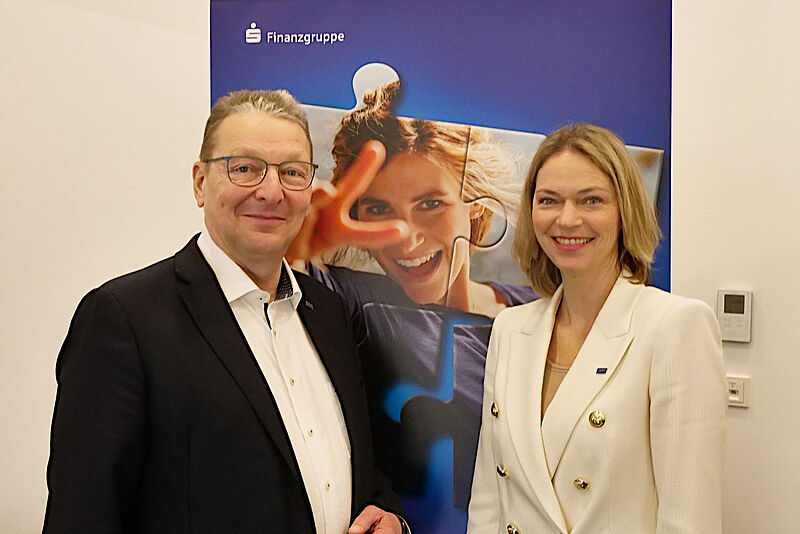 Alexander Piwonski und Mareike Steinmann-Baptist von der Union Reiseversicherung stehen nebeneinander vor einer Werbewand der Versicherung.
