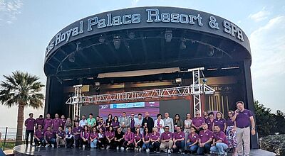 Auf der Bühne stehen zahlreiche Bentour-Mitarbeiter, in lila gekleidet, zusammen mit Reisebüro-Partnern, die einen Preis gewonnen haben, im Hintergrund blauer Himmel und Palmen.