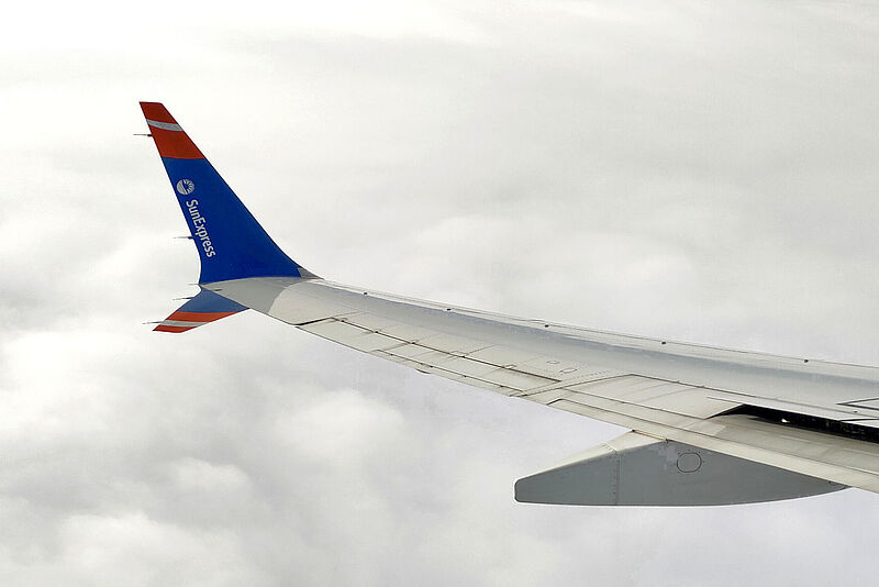 Ein Winglet und Ausschnitt einer Tragfläche eines Flugzeugs von Sun Express mit Firmenlogo vor einer weißen Wolkenwand.