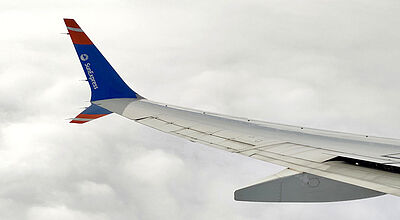 Ein Winglet und Ausschnitt einer Tragfläche eines Flugzeugs von Sun Express mit Firmenlogo vor einer weißen Wolkenwand.