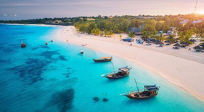Luftaufnahme der Fischerboote an der tropischen Meeresküste mit weißem Sandstrand bei Sonnenuntergang. Sommerurlaub am Indischen Ozean, Sansibar. Landschaft mit Boot, Palmen, transparentes blaues Wasser.