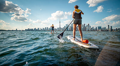 Zwei Personen in Rückansicht paddeln auf die Skyline von Toronto zu