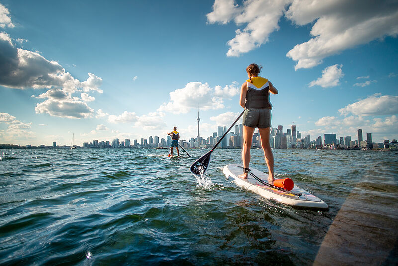 Zwei Personen in Rückansicht paddeln auf die Skyline von Toronto zu