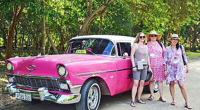 Schulungen vor Ort haben den meisten Output für Reiseverkäufer, hier Teilnehmer vom Campus Live Bienvenido Kuba Drei sommerlich bekleidete Damen stehen vor einem pinkfarbenen Oldtimer