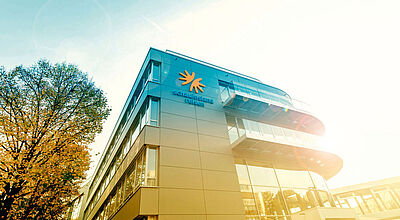 Der Firmensitz von Schauinsland-Reisen mit Logo an der Außenwand, Sonne fällt von rechts ins Bild, auf der linken Seite ein herbstlicher Laubbaum