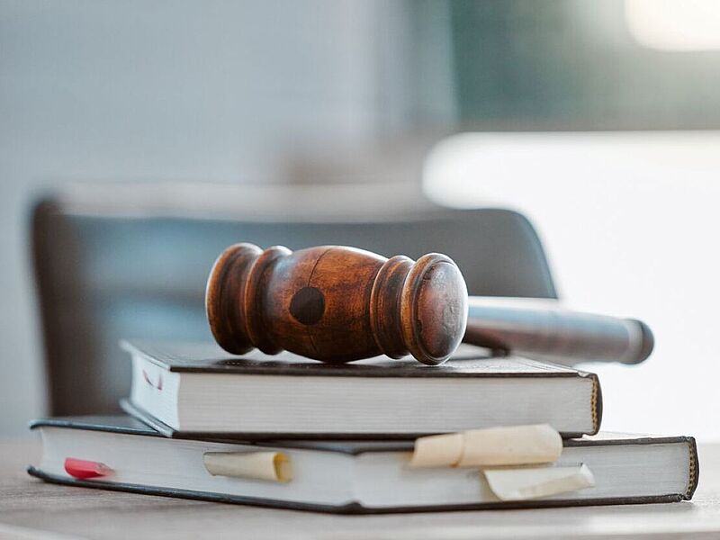 In zwei Fällen ziehen nun Kunden von FTI gegen stationäre Reisbüros vor Gericht. Foto: iStock/Jacob Wackerhausen Ein Richterhammer liegt auf zwei gestapelten Gesetzbüchern auf einem Schreibtisch, im Hintergrund ist unscharf ein Stuhl und ein Fenster zu sehen.