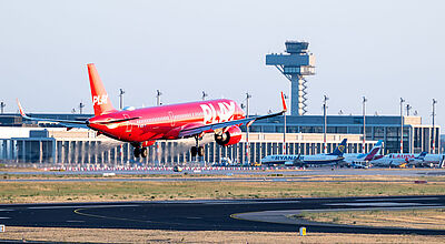 Wegen schlechter Geschäftszahlen stellt Play – hier am Flughafen BER – auch die Deutschland-Strecken ein. Foto: Günter Wicker/Flughafen Berlin Brandenburg Ein rotes Flugzeug der isländischen Billigfluggesellschaft Play landet am Berliner Flughafen. Im Hintergrund sind Terminalgebäude und Tower zu sehen.