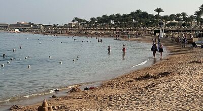 Makadi Bay südlich von Hurghada: Das Reiseziel ist im laufenden Winter das Topreiseziel von TUI Deutschland. Das Bild zeigt einen Strand in Ägypten, Spaziergänger laufen an der Wasserlinie entlang, Schwimmer im Meer und Liegen an den Stränden. Im Hintergrund eine Hotelanlage.