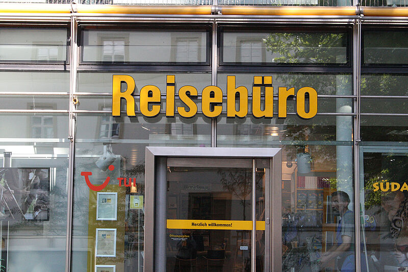Glasfront eines Reisebüros. Über der Eingangstür steht in gelben Buchstaben das Wort Reisebüro.