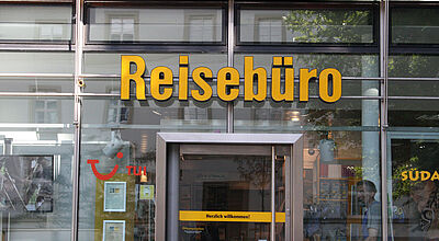 Glasfront eines Reisebüros. Über der Eingangstür steht in gelben Buchstaben das Wort Reisebüro.