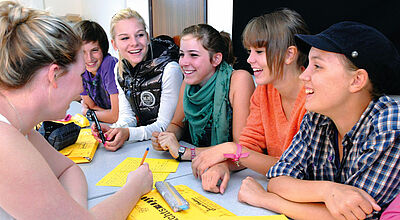Gruppe von lachenden weiblichen Teenagern sitzt um einen Tisch