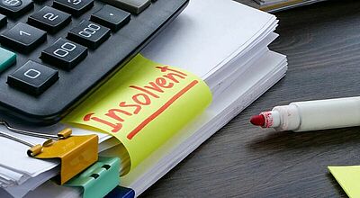 Taschenrechner auf einem Stapel Papieren mit dem Wort insolvent