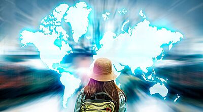 Eine Person mit Rucksack und Hut blickt auf eine leuchtend blaue Weltkarte, die sich vor ihr ausbreitet – Symbol für globale Reisemöglichkeiten und digitale Reiseinspiration.