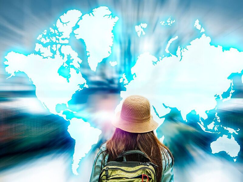 Wohin geht die Reise? Auf der Reiseplattform Mindtrip liefert die KI Inspiration – und TUI die passenden Angebote. Foto: Chan2545/iStock Eine Person mit Rucksack und Hut blickt auf eine leuchtend blaue Weltkarte, die sich vor ihr ausbreitet – Symbol für globale Reisemöglichkeiten und digitale Reiseinspiration.