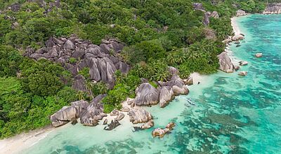 Luftaufnahme eines Seychellen-Strandes mit markanten grauen Granitfelsen, türkisfarbenem Wasser und tropischer Vegetation.