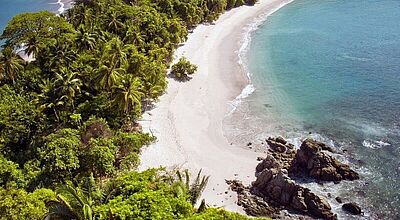 Luftaufnahme eines tropischen Strandes im Manuel-Antonio-Nationalpark in Costa Rica mit dichtem Regenwald, weißem Sandstrand und türkisfarbenem Meer.