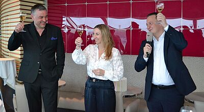Aida-Trio beim Empfang von Vertriebspartnern (von links): Alexander Ewig, Senior Vice President Marketing & Sales, Steffi Heinicke, SVP Guest Experience, und Präsident Felix Eichhorn. Foto: ck In der Lounge eines Aida-Kreuzfahrtschiffes prosten sich bei einem Geschäftsempfang drei strahlende Verantwortliche der Reederei mit gefüllten Sektgläsern zu.