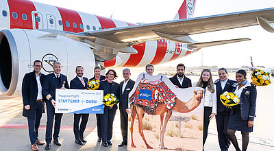 Die Bordcrew eines Condor-Flugzeugs steht mit einem Schild, auf dem „Inaugural Flight Stuttgart – Dubai“ steht, sowie einem Aufsteller, auf dem ein Kamel abgebildet ist, vor einem Flugzeug von Condor auf dem Vorfeld des Flughafens Stuttgart.