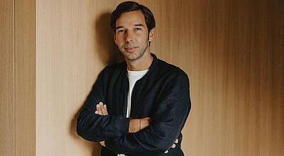 Sieht in verantwortungsvollem Wirtschaften und gesellschaftlichem Engagement keinen Widerspruch: Ambros Gasser, Geschäftsführer von ASI Reisen. Foto: ASI Reisen Ein Mann mittleren Alters steht vor einer holzvertäfelten Wand, mit verschränkten Armen und leichtem Lächeln, gekleidet in einer dunklen Jacke und einem weißen T-Shirt.