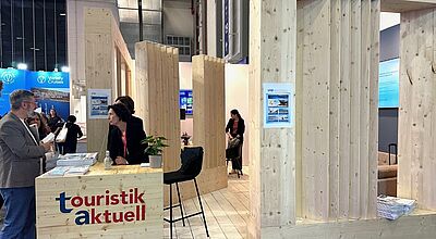 Ein Messestand ganz aus Holz an dem drei Personen sind