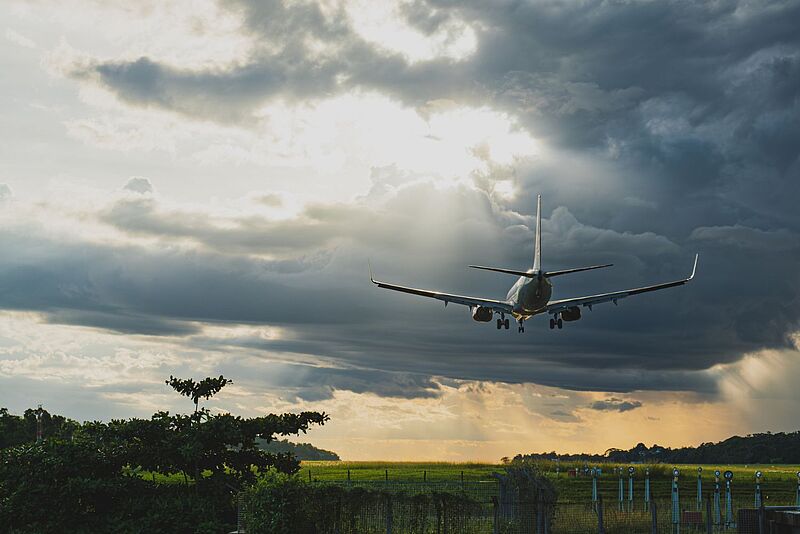Flugzeug bei der Landung unter dramatischem Wolkenhimmel mit Sonnenstrahlen.