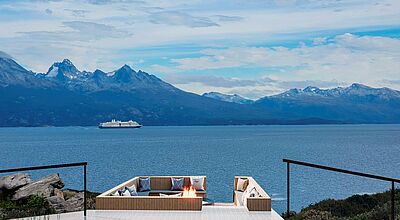 Luxuriöse Terrasse mit Feuerstelle und Panoramablick auf ein Kreuzfahrtschiff im Beagle-Kanal vor schneebedeckten Anden in Patagonien – exklusives Reiseziel für Natur- und Kreuzfahrtliebhaber in Südamerika