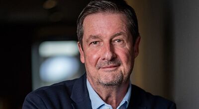 Carsten Burgmann ist neuer Sprecher der Geschäftsführung von Suedwest Touristik Porträt eines Mannes mittleren Alters in Businesskleidung. Er trägt ein dunkelblaues Sakko über einem hellblauen Hemd, steht mit verschränkten Armen an eine Wand gelehnt und blickt ruhig in die Kamera. Der Hintergrund ist unscharf und wirkt wie ein Innenraum mit gedämpftem Licht.