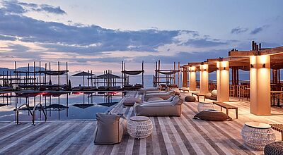 Stimmungsvolle Poolterrasse eines Luxusresorts auf Kreta bei Sonnenuntergang, mit gemütlichen Loungemöbeln, beleuchteter Pergola und Blick auf das Meer