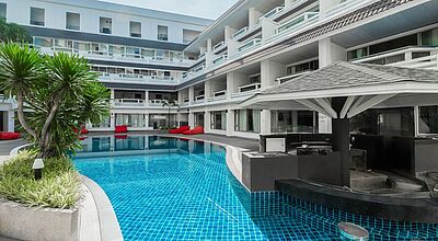 Weißes mehrstöckiges Gebäude, in dessen Innenhof ein Pool liegt.