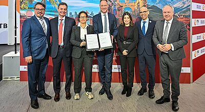 Vier Männer im Anzug und zwei Frauen in Dienstkleidung zeigen einen Vertrag