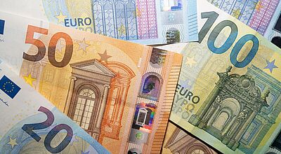 Nahaufnahme von Euro-Geldscheinen, die versetzt übereinander liegen. Erkennbar sind ein 20-Euro-, ein 50-Euro- und ein 100-Euro-Schein