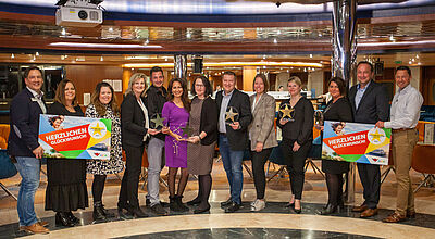 Der Smiling Star Award von Aida wurde letztmals 2019 verliehen. Foto: Aida Cruises Eine Gruppe von Touristikern hat sich zu einem Gruppenfoto in der Lobby eines Kreuzfahrtschiffes nebeneinander aufgestellt