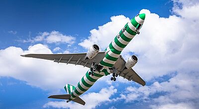 Eine grün-weiß geringelte Condor-Maschine vom Typ Airbus A330 Neo von unten vor blauem Himmel mit weißen Wolken fotografiert.
