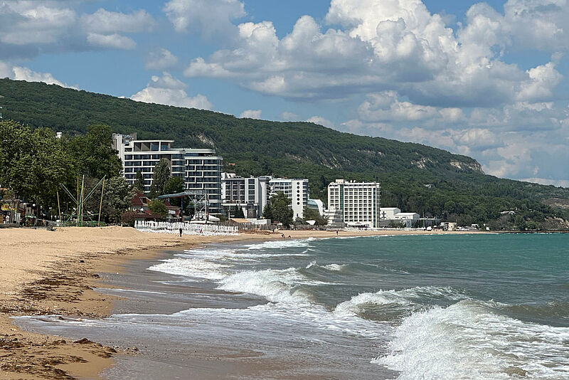 Goldstrand bei Varna: In Teilen Partyhochburg, in vielen Abschnitten ruhig und entspannt. Foto: mg Panoramablick auf den Goldstrand in Bulgarien mit sanften Wellen, goldenem Sandstrand, modernen Hotels und grünen Hügeln im Hintergrund unter blauem Himmel – Urlaubsparadies an der Schwarzmeerküste.