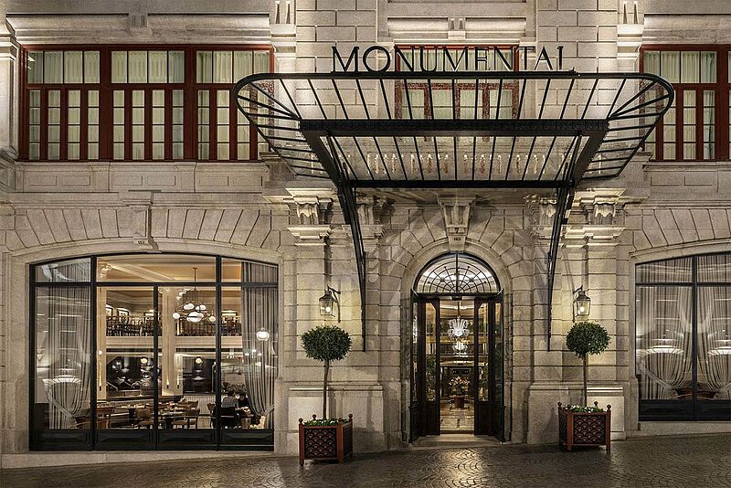 Eingangsbereich des The One Monumental Palace in Porto mit beleuchteter Fassade im neoklassizistischen Stil und Glasvordach über dem Hoteleingang.