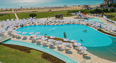 Pool des Sunrise Magic Resort umgeben von weißen Sonnenschirmen, im Hintergrund der Strand und das Meer