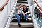 Zwei Frauen sitzen auf einem Kreuzfahrtschiff auf einer Treppe und lächeln in die Kamera