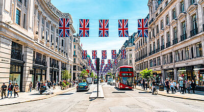 Straße in London mit Fahnen von Großbritannien, einem roten Sightseeing Bus und Leuten